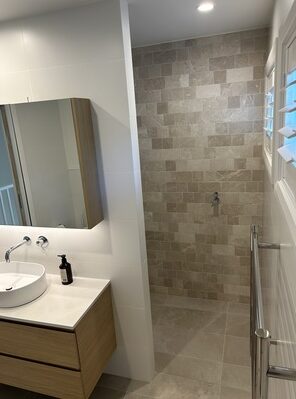Contemporary bathroom vanity with a circular mirror, wall-mounted faucet, and beige tile backsplash.
