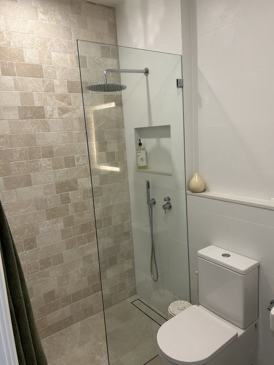 A modern bathroom with a glass-enclosed walk-in shower, beige tiles, and a white toilet